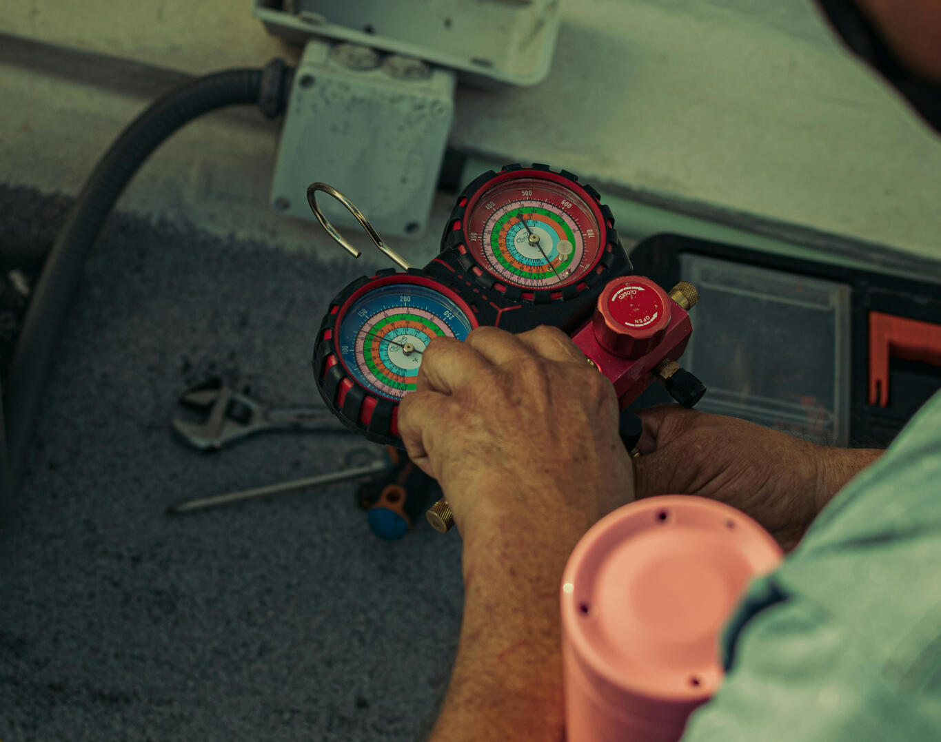 Technician Adjusting HVAC Pressure Gauges A technician using red pressure gauges to inspect and adjust an HVAC system, with tools and cables visible in the background.