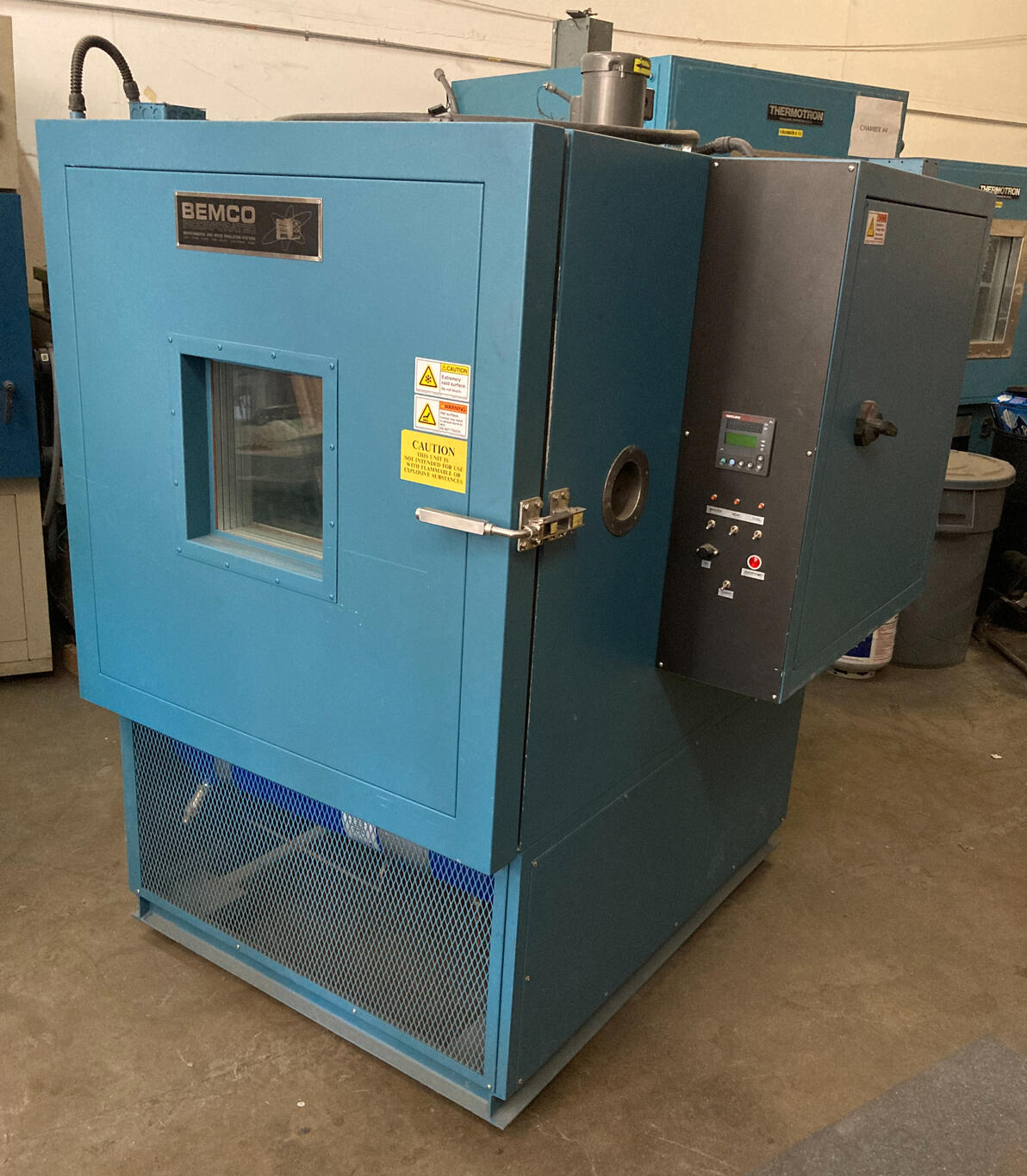 BEMCO Environmental Test Chamber A blue BEMCO environmental test chamber used for temperature and humidity testing, equipped with a viewing window and control panel, positioned in an industrial workshop.